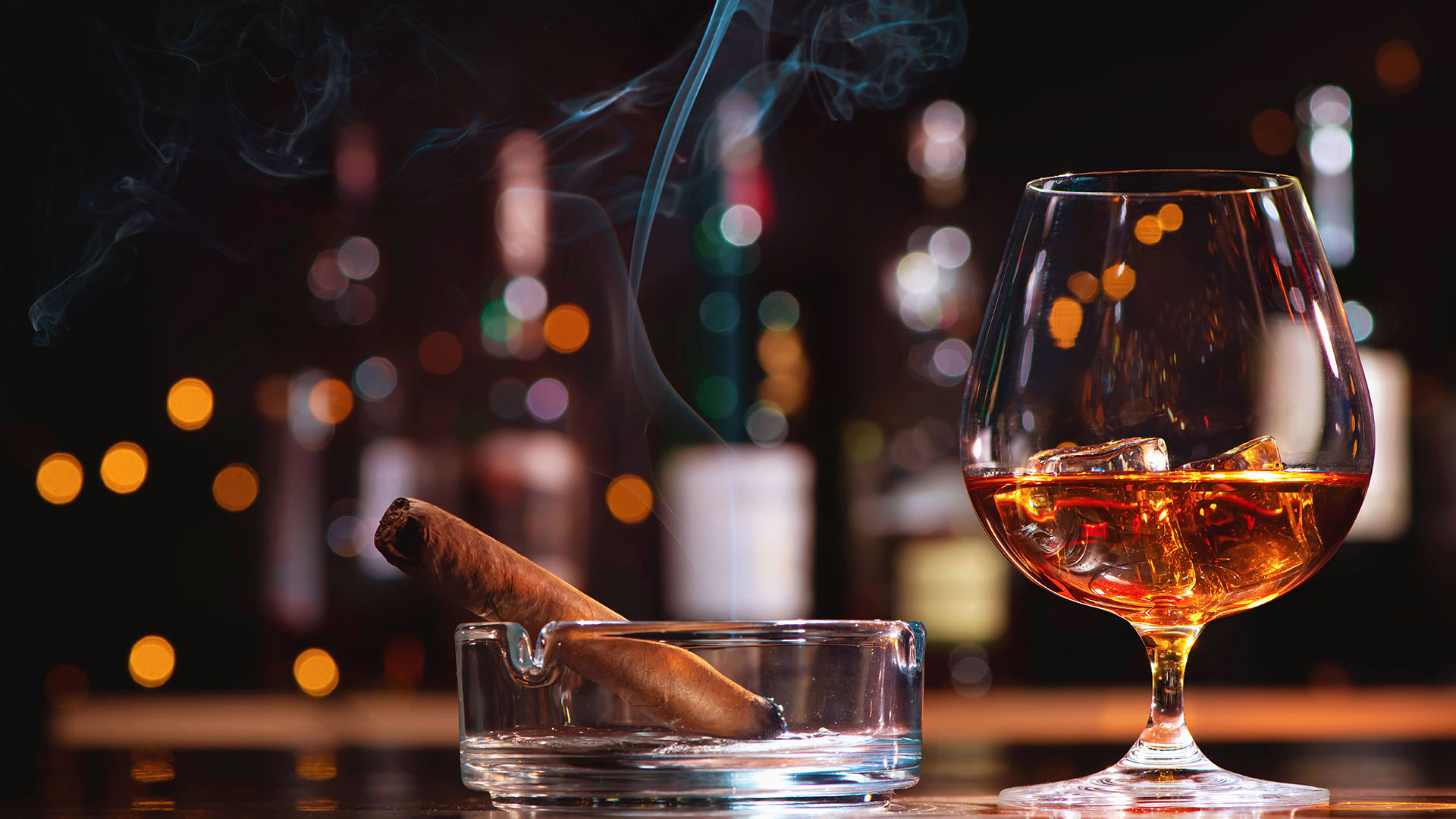 Glass of whiskey or cognac with ice cubes and smoking cigar